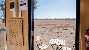 A room with a door leading to an outdoor area with a table and chairs, a fire extinguisher, and a thermostat on the wall.