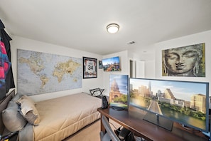 Un dormitorio con una cama, un escritorio con una computadora, un mapa mundial y cuadros enmarcados.