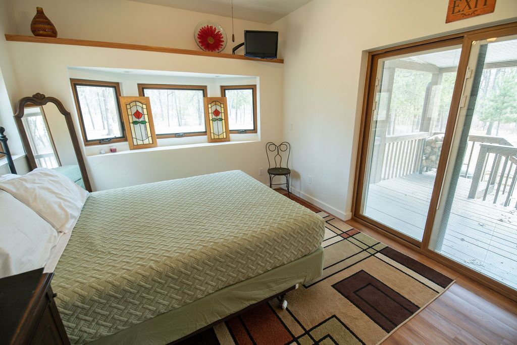 A bedroom with a bed, a TV, a window with a view, and a door to a balcony.