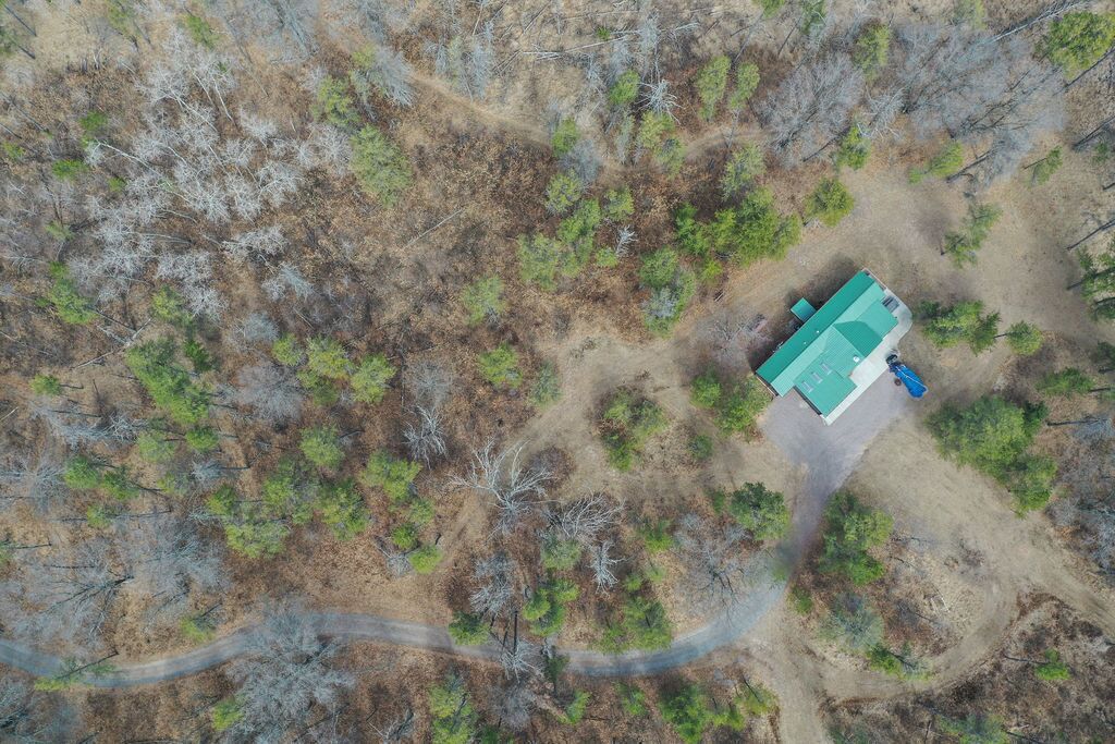 Vista aèria d'una cabana amb teulada verda, envoltada per una zona boscosa amb un camí de terra que hi condueix.