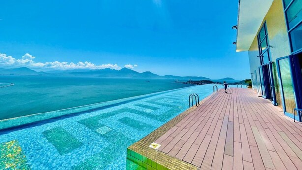 A poolside area with a wooden deck and a view of the sea and mountains. - Dana Pearl Bay Apartment by Dimo Trip (Da Nang)