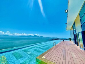 A poolside area with a wooden deck and a view of the sea and mountains. - Dana Pearl Bay Apartment by Dimo Trip (Da Nang)