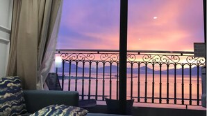 A balcony with a view of a sunset over a body of water and mountains. - Dana Pearl Bay Apartment by Dimo Trip (Da Nang)
