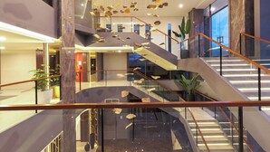 Un interior moderno con una escalera central, barandillas de cristal y un techo con elementos decorativos colgantes.