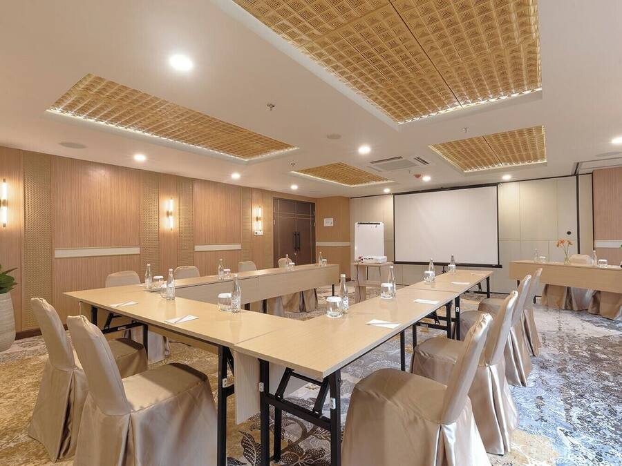 A conference room with long tables, chairs, and a projector screen.