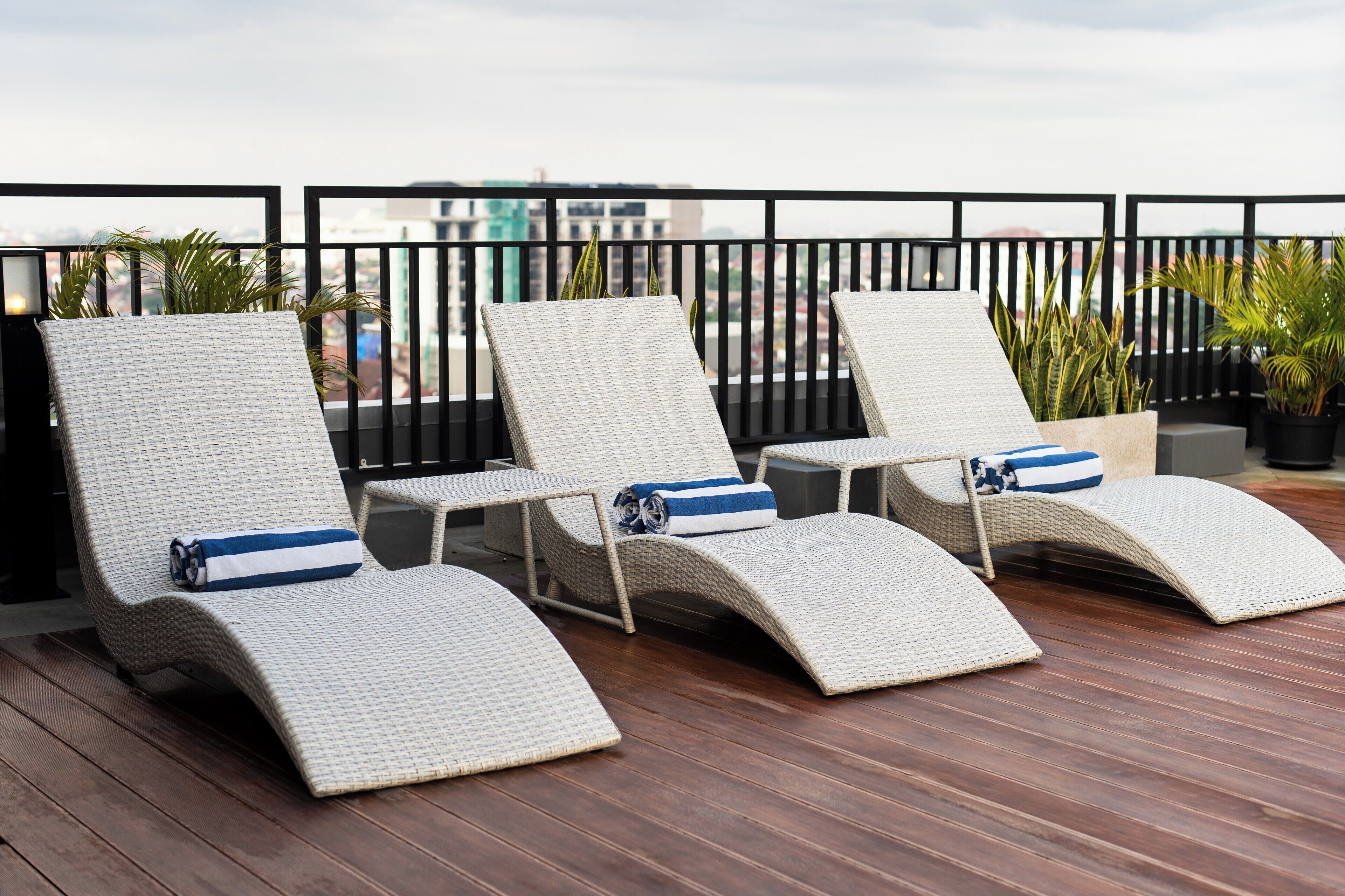 A rooftop terrace with three wicker lounge chairs, each with a blue-striped pillow.