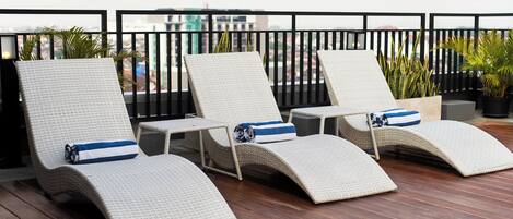 Una terraza en la azotea con tres sillones de mimbre, cada uno con un cojín a rayas azules.
