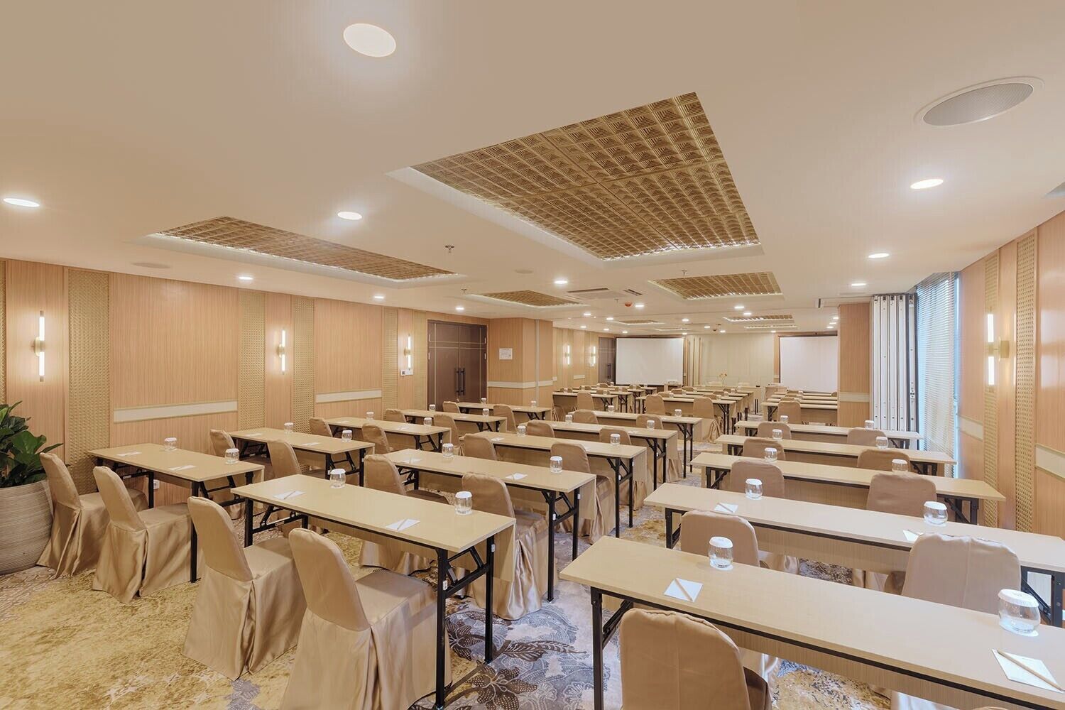 A conference room with multiple tables and chairs, equipped with water bottles, and a projector screen.