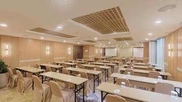 A conference room with multiple tables and chairs, equipped with water bottles, and a projector screen.