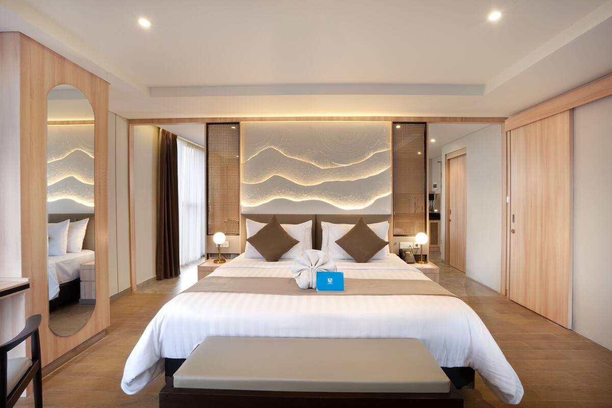 A modern hotel room with a large bed, bedside tables, a bench, and a wall with a wave-like design.