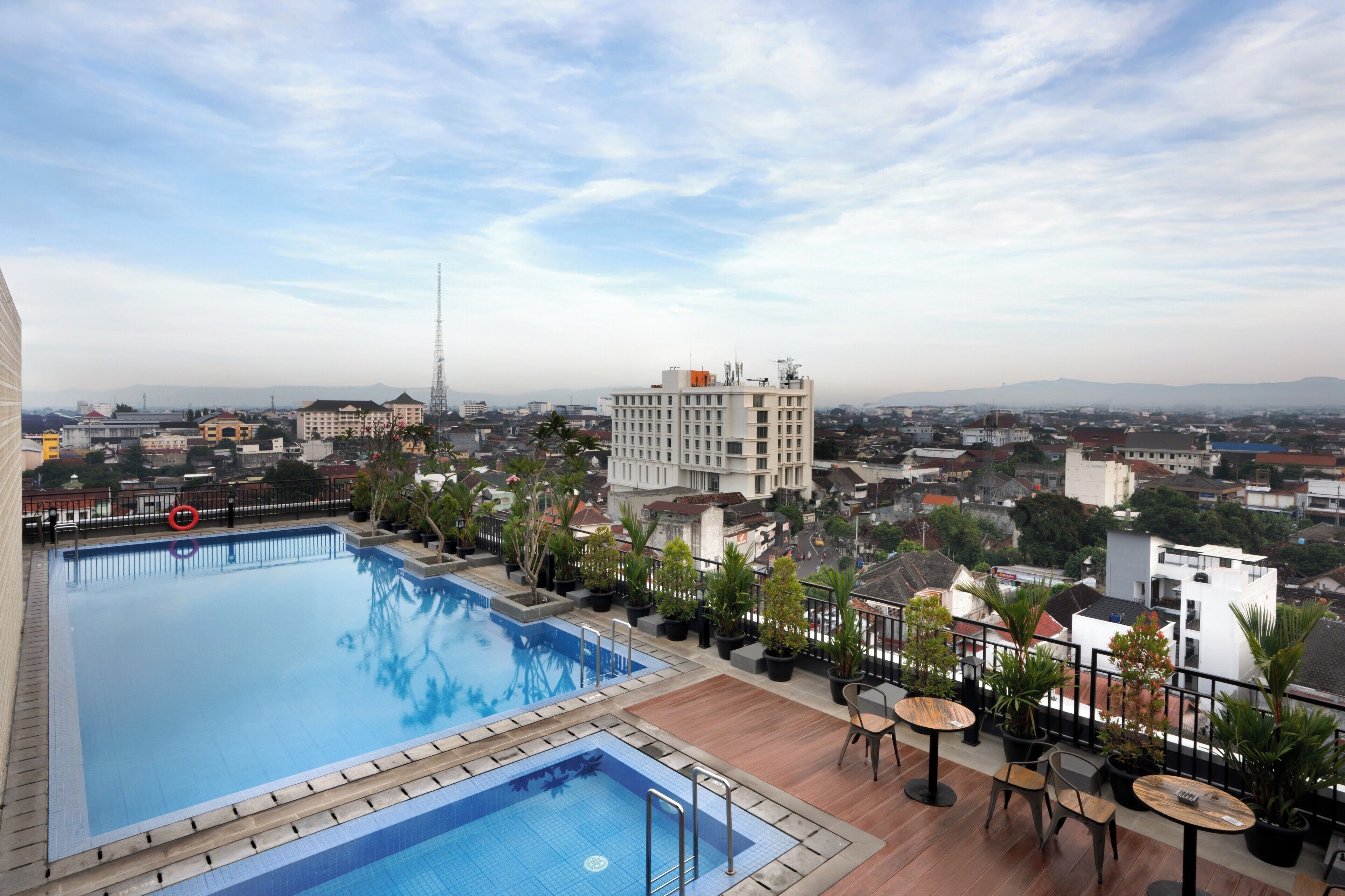 A rooftop swimming pool with a view of the cityscape, including a prominent building and surrounding residential areas.