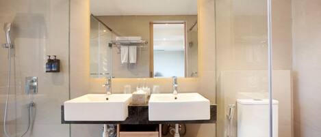 A modern bathroom with two sinks, a glass shower enclosure, and a toilet.