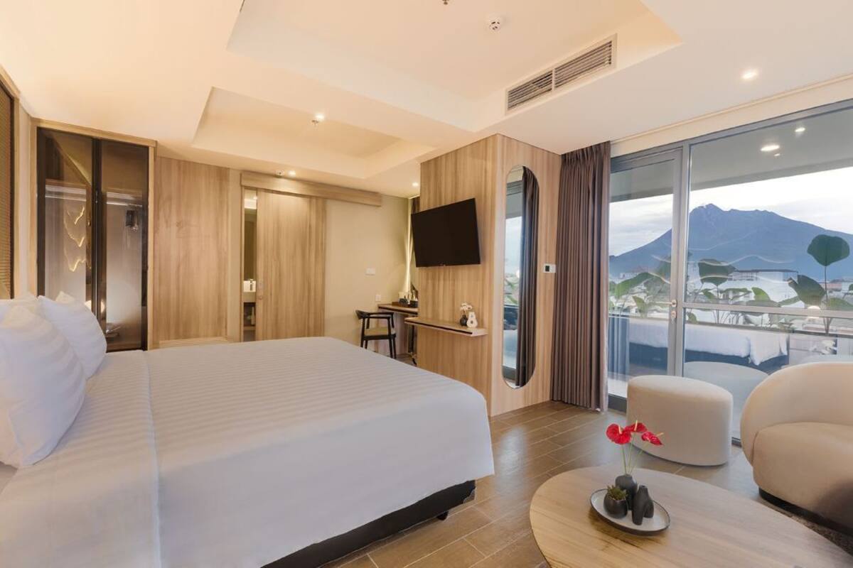 A modern hotel room with a large bed, a desk, a flat-screen TV, and a balcony with a mountain view.