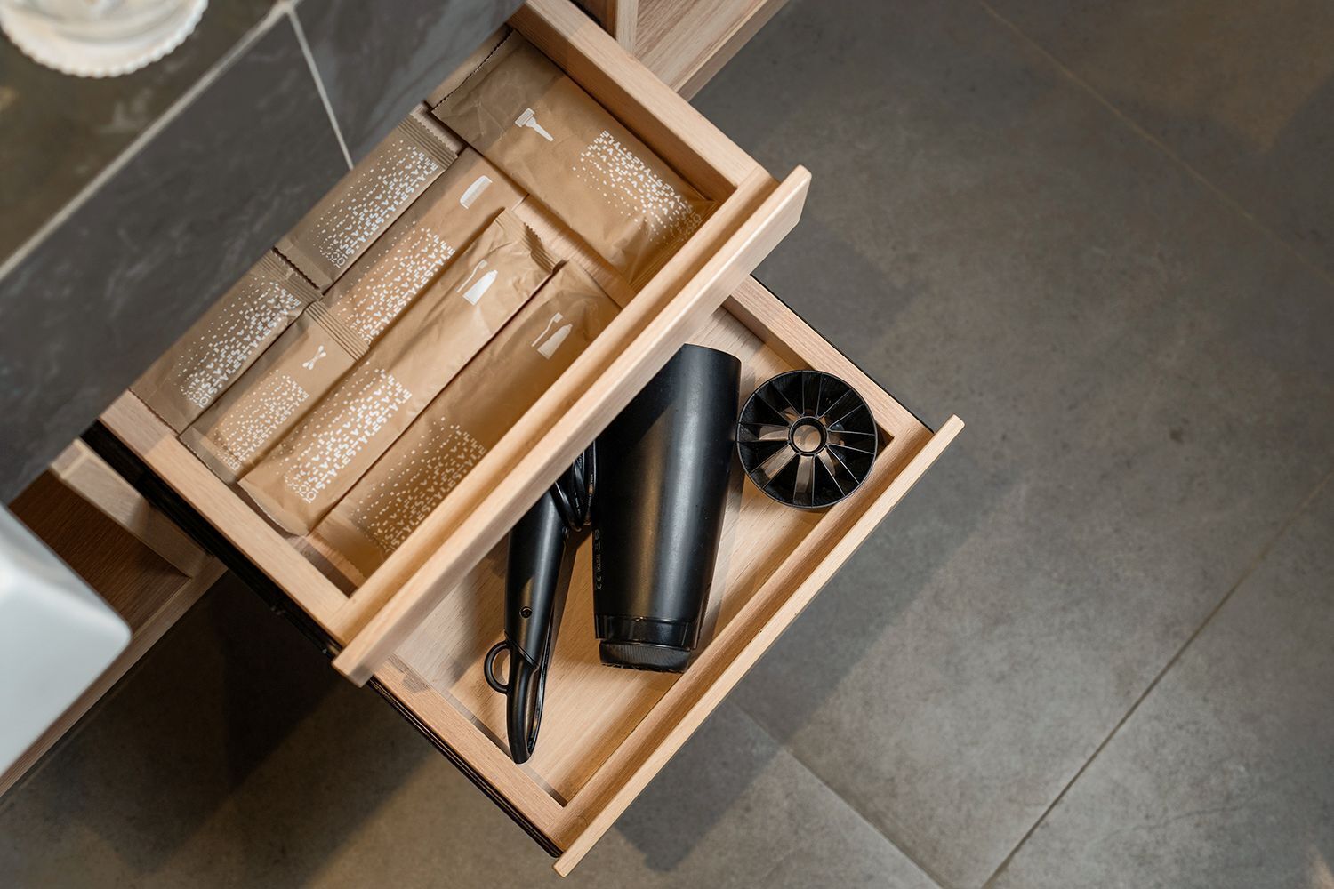 A wooden drawer with a black hairdryer, a black cylindrical object, and a black circular object.
