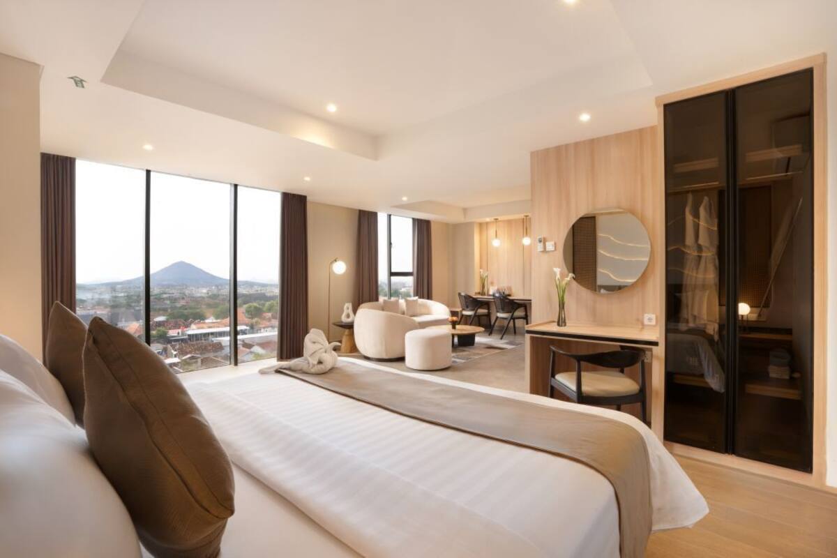 A modern hotel room with a large bed, a desk, a chair, and a view of the city.