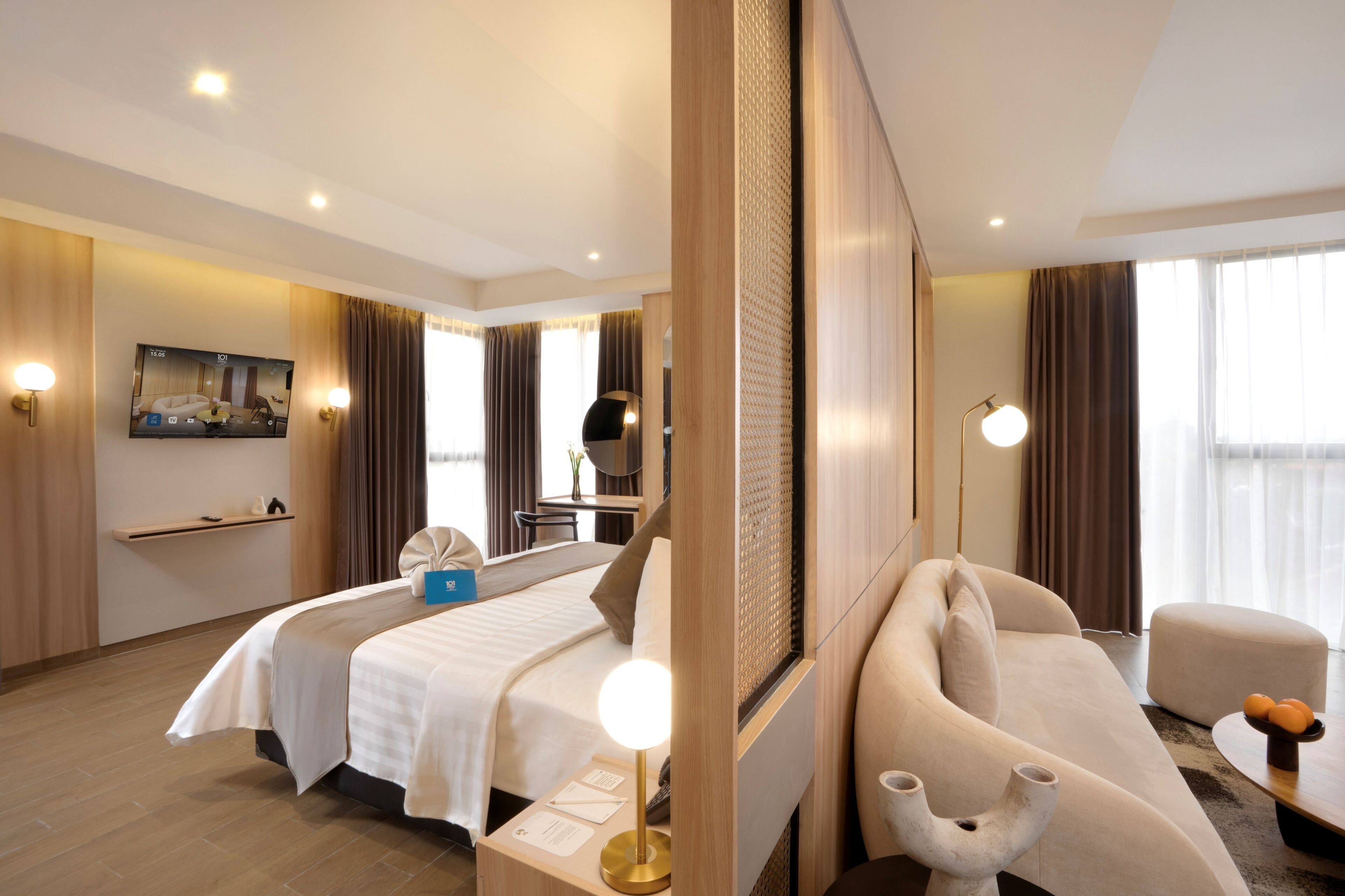 Ein modernes Hotelzimmer mit zwei Betten, einem Sofa, einem Schreibtisch und einem Fernseher.