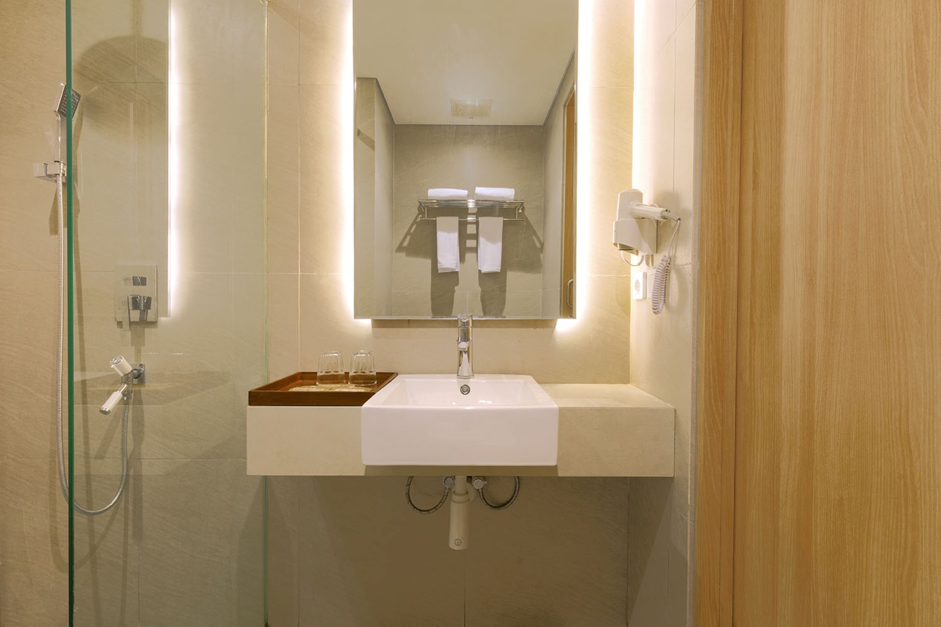 A modern bathroom with a glass-enclosed shower, a white sink with a wooden tray, and a mirror above the sink.