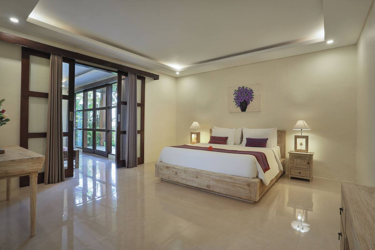 A spacious bedroom with a large bed, bedside lamps, and a view through an open door.