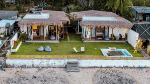 Propiedad frente a la playa con construcciones de techo de paja, una playa arenosa y palmeras.