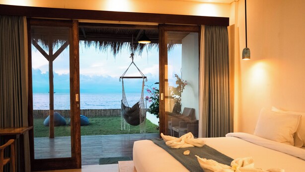 Un dormitorio con cama, una silla colgante y vista al mar.