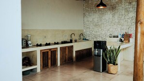 Una cocina con pared de piedra, armarios de madera, pileta integrada, refrigerador e iluminación colgante.