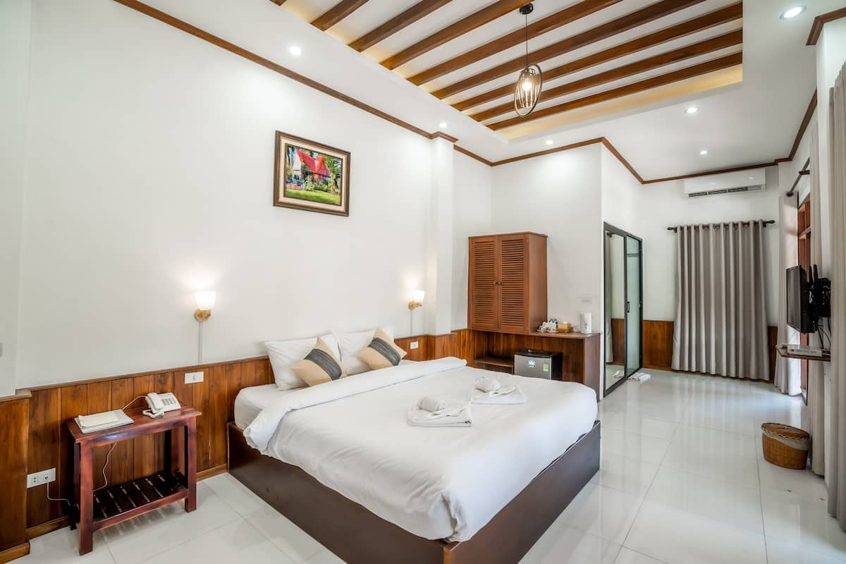 Habitación de hotel con una cama grande, cabecera de madera, mesitas de noche, un teléfono y un cuadro en la pared.