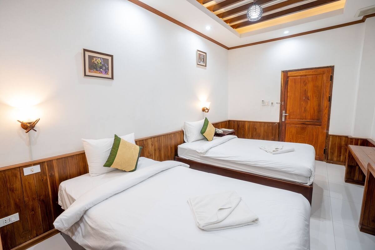 Habitación de hotel con dos camas, cabeceros de madera, ropa de cama blanca e iluminación fijada a la pared.