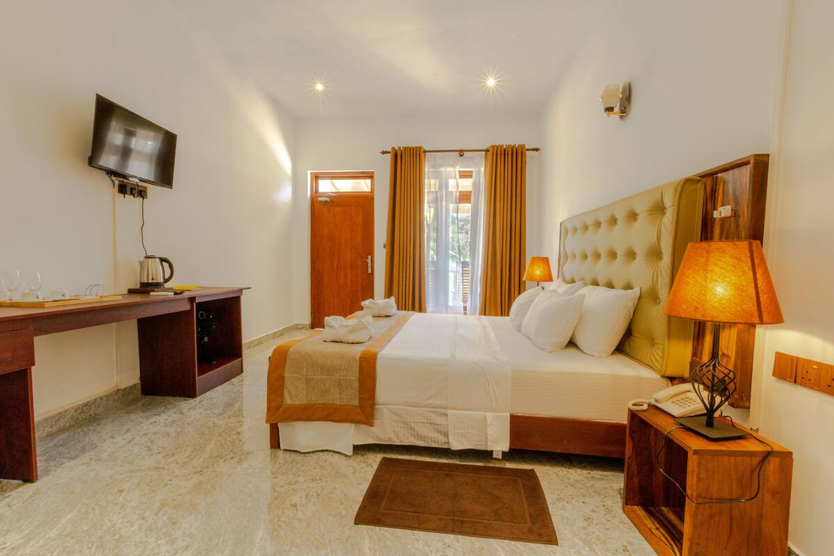 Quarto de hotel com cama, escrivaninha, televisão e abajur.