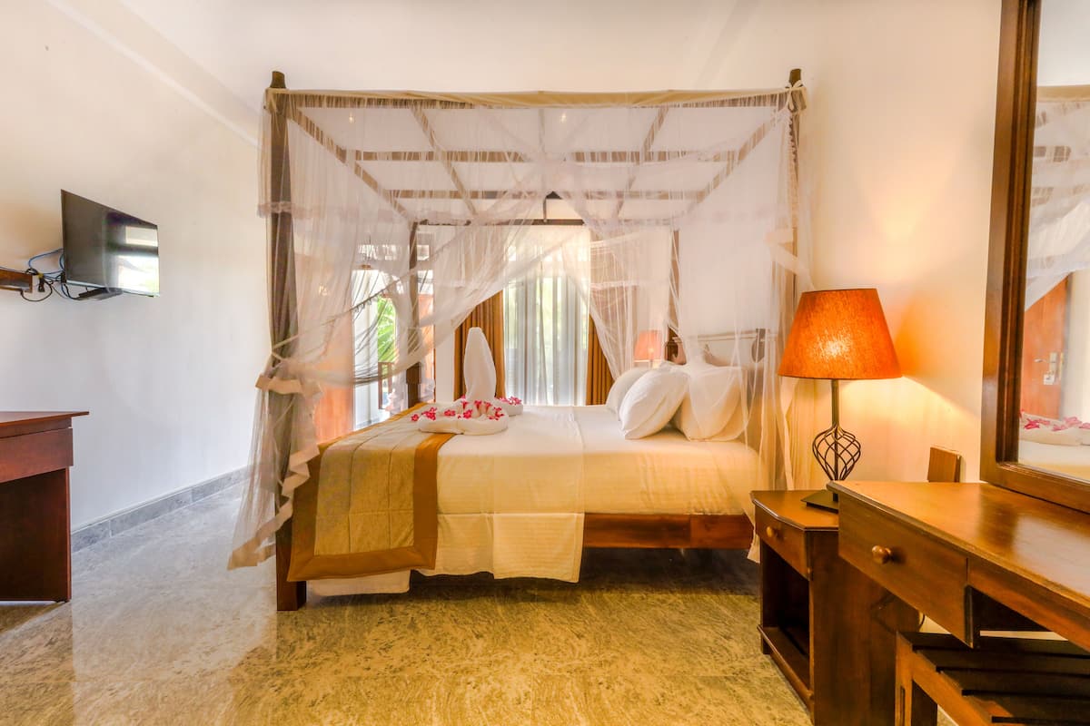 Quarto com cama de dossel, mesa de cabeceira, luminária e TV fixada na parede.