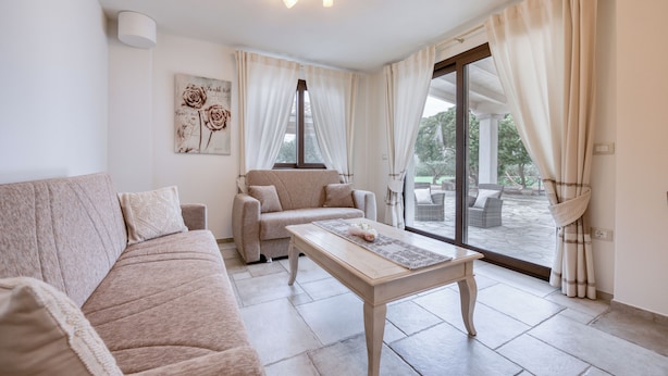 Ein Wohnzimmer mit beiger Couch, einem Couchtisch und einem großen Fenster mit Vorhängen.