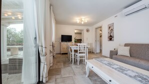 Ein geräumiger Wohnbereich mit einer Couch, einem Esstisch mit Stühlen, einem Fernseher und einer Küche im Hintergrund.
