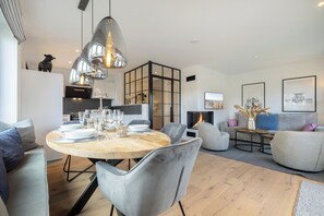 Enjoy meals with family and friends at the central dining table, surrounded by comfortable seating and a warm fireplace.