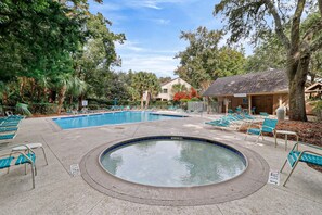 Ein Swimmingpool mit Liegestühlen und Whirlpool, umgeben von Bäumen und einem Gebäude.