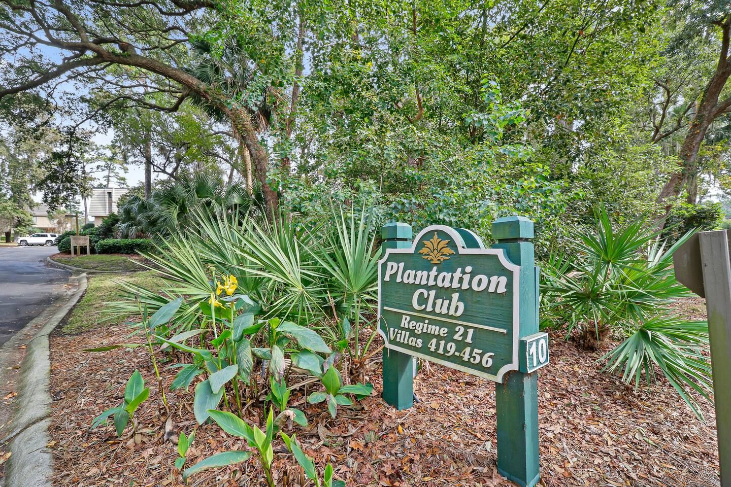 Une enseigne indiquant « Plantation Club », avec le chiffre 10, entourée d’une végétation luxuriante et avec une route en arrière-plan.