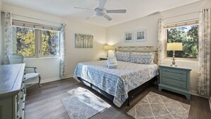 Un dormitorio con cama, escritorio, silla, mesita de noche y ventana con cortinas.