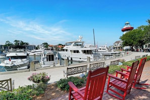 A marina with several yachts docked, a lighthouse in the background, and red chairs in the foreground.