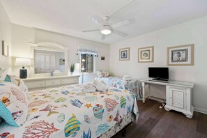 Une chambre avec deux lits, un ventilateur de plafond, une télévision et un bureau avec un ordinateur.