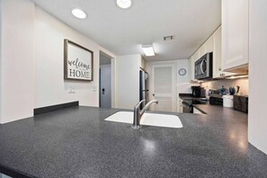 A modern kitchen with a granite countertop, stainless steel faucet, and a clock on the wall.
