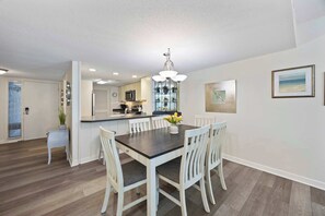 Une cuisine moderne avec des meubles blancs, un îlot central et un coin repas comprenant une table en bois foncé et des chaises blanches.