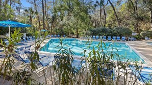 Una piscina rodeada de sillas de descanso y sombrillas, con árboles al fondo.