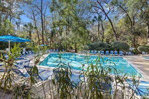 Una piscina circondata da lettini e ombrelloni, con alberi sullo sfondo.