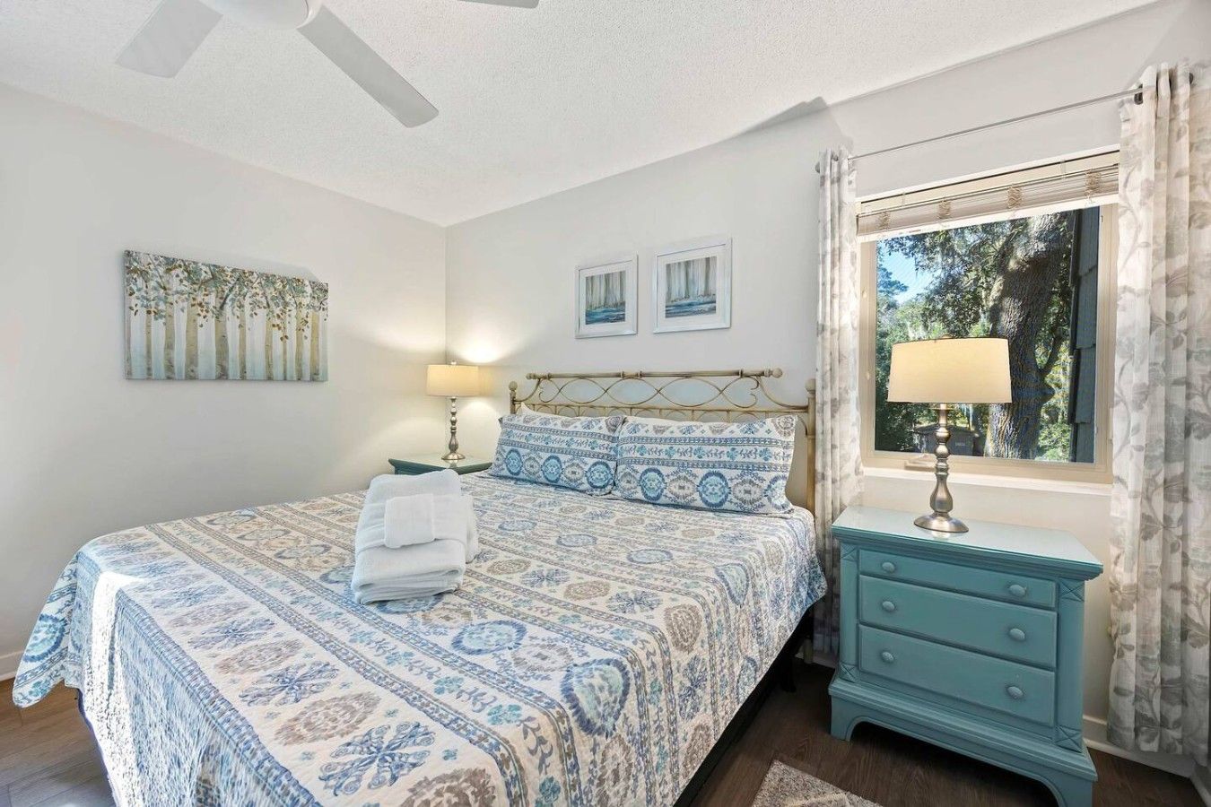 A bedroom with a bed, a nightstand, a window with curtains, and wall art.