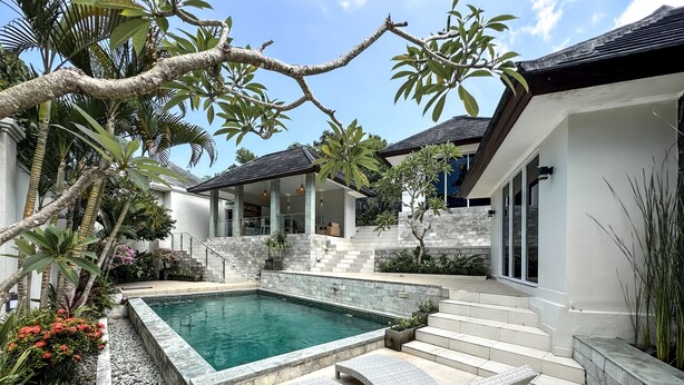 A modern outdoor pool area with stone steps leading to a covered seating area, surrounded by lush greenery and a clear blue sky. - MaySa Villa Uluwatu (Pecatu)