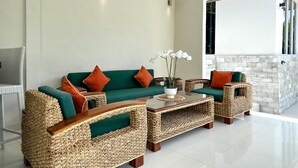 A modern living room with wicker furniture, a green sofa with orange cushions, and a coffee table with a potted orchid. - MaySa Villa Uluwatu (Pecatu)