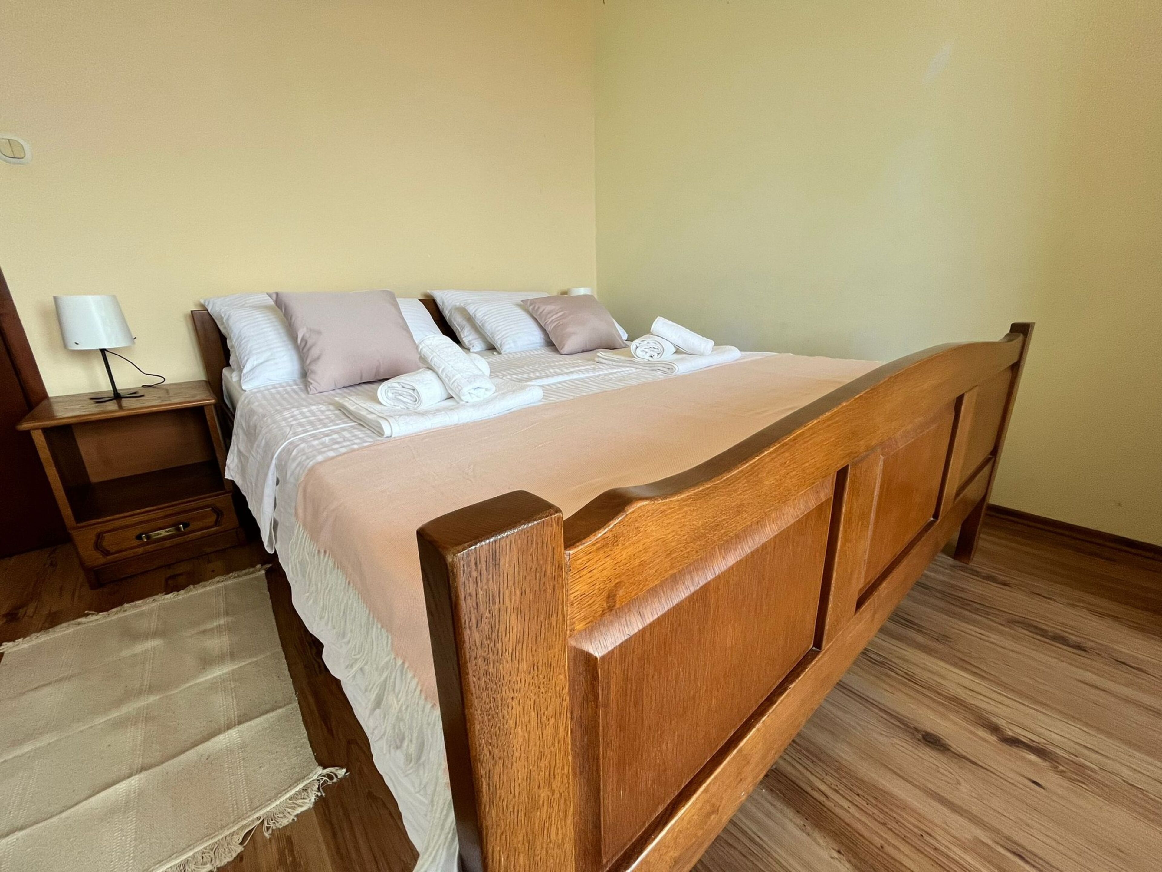 Un lit bien fait avec une tête de lit en bois, une table de chevet avec une lampe et un plancher en bois.