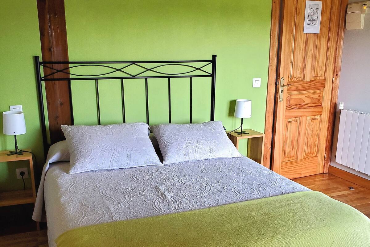 Un lit avec une tête de lit en bois, deux tables de chevet avec des lampes, un mur vert et une porte en bois.