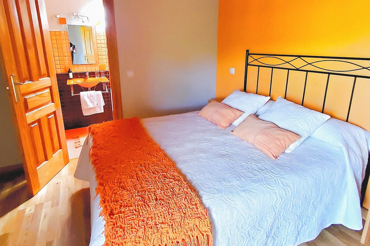 Une chambre à coucher avec un lit, une porte en bois et une salle de bain visible à travers une porte ouverte.