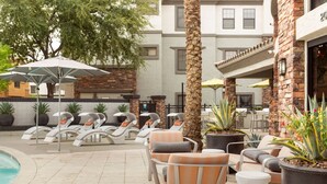 A poolside area with lounge chairs and umbrellas, a palm tree, and a building with a stone facade. - CozySuites Glendale with pool  04 and 18 (Glendale)
