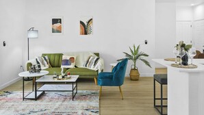 A modern living room with a green sofa, a blue armchair, a coffee table, and a small dining area with a white table and chairs. - CozySuites Glendale with pool  04 and 18 (Glendale)