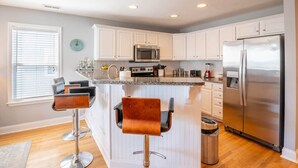 A modern kitchen with white cabinets, stainless steel appliances, and two bar stools.